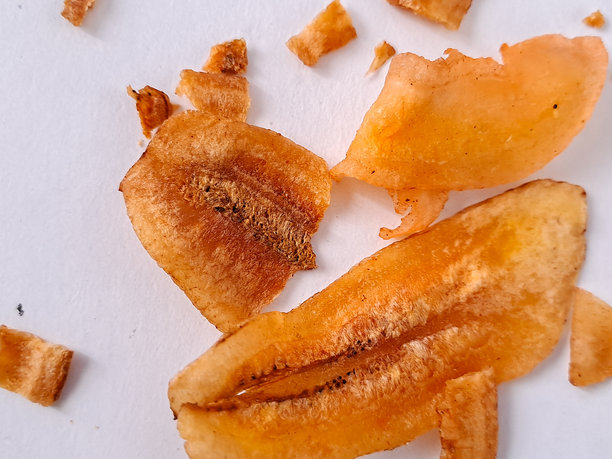 三片干香蕉片的照片，背景为纯白色。这些香蕉片呈现出丰富的金橙色，表面有干燥过程留下的明显纹理。香蕉中的天然糖分已经焦糖化。图片下载