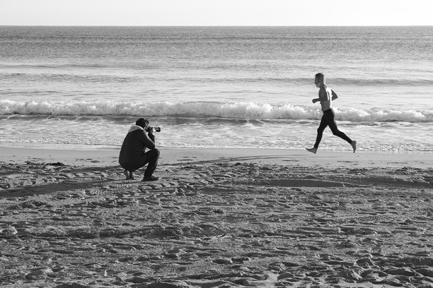 女人在冬季早晨的阿雷纳莱斯德尔索尔海滩拍摄年轻男子奔跑的照片图片下载