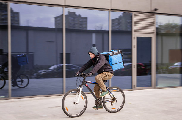 年轻的外卖送餐员穿着连帽衫，正在骑自行车前往快餐店，准备取餐进行送餐 - 股票照片图片下载