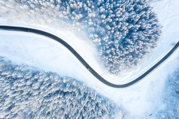 冬季时分的蜿蜒道路和森林的鸟瞰图。森林被雪覆盖。空中拍摄的自然冬季风景。适合明信片、背景和壁纸的照片。图片下载