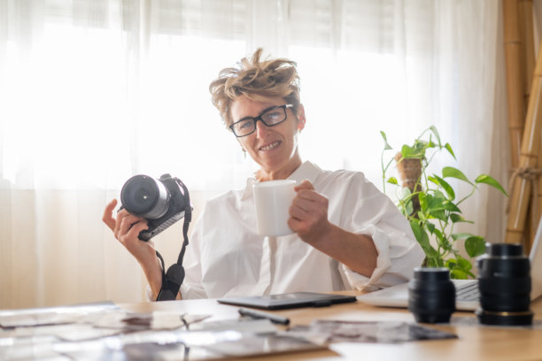 专业摄影师在家中工作空间放松，享用咖啡，周围充满相机设备和照片打印，营造出宁静的工作环境图片下载