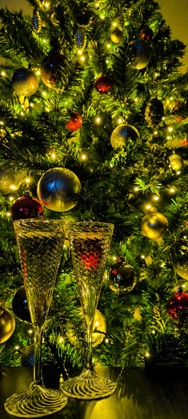 装饰有球和其他装饰品的圣诞树背景下的香槟酒杯。竖版照片图片下载