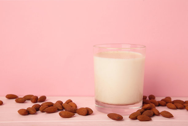 粉色背景上的新鲜杏仁奶和杏仁。健康的植物基替代牛奶。竖版照片。图片下载
