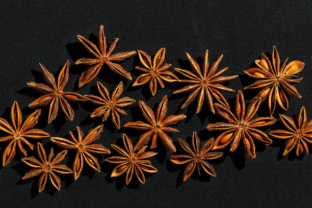阳光下的棕色八角星图案，俯视特写，香气四溢的干茴香种子，黑色背景，极简美学食品，质感图形照片，自然调味品。图片下载