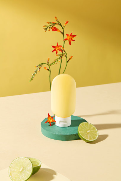 护肤产品广告照片模板。正面视角的黄色瓶子模型，放置在绿色底座上，背景为黄色。周围有橙色花朵和两片柠檬。图片下载