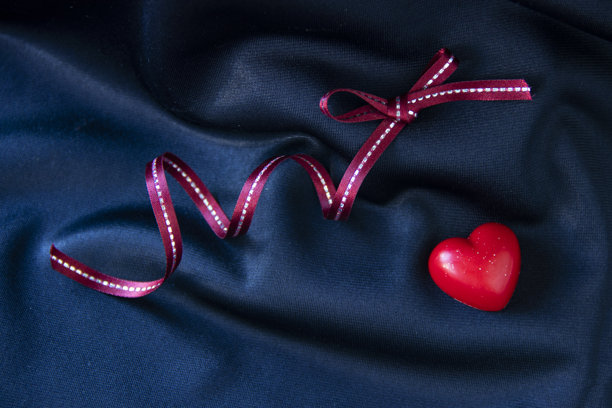 情人节图片。红色巧克力心形与粉色丝带，背景为深蓝色布料。图片下载