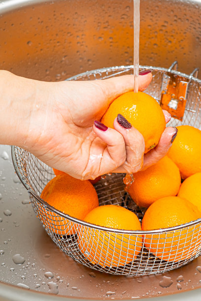 女人在厨房用漏网洗橘子，竖版照片图片下载