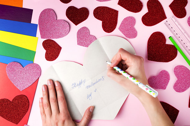 女人的手在纸心上写下情人节祝福。情人节卡片手工制作的DIY概念。俯视图。平铺展示。逐步照片说明。第11步。图片下载