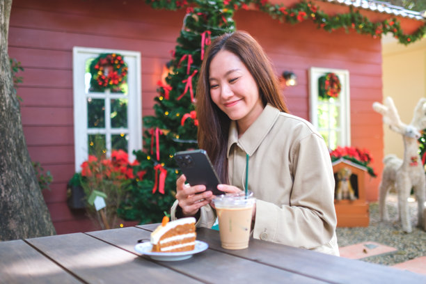 圣诞派对上，一位女性手持手机和一杯咖啡，桌上还有一块蛋糕的肖像照片图片下载