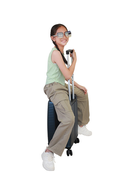 亚洲女孩坐在行李箱上，摆姿势并直视镜头，佩戴着太阳镜，背景为白色。儿童时尚与旅行概念。全身照片。图片下载