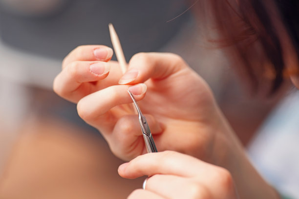 女性用小剪刀修剪指甲边缘，强调指甲护理和美丽。这张图片捕捉了美甲和个人护理的精髓。图片下载
