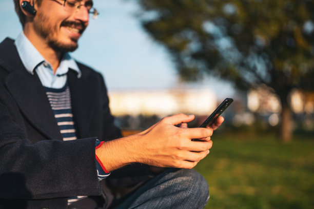 身穿外套、戴着眼镜和入耳式耳机的商人在户外使用手机的特写照片图片下载