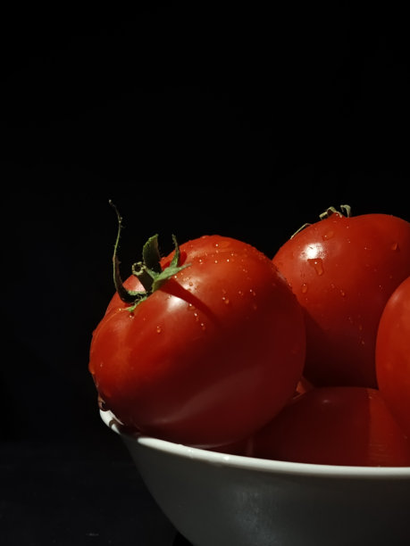 黑色背景上的水滴番茄。多汁的红番茄与叶子放在白色盘子里。昏暗的照片。广告背景，留有文字空间。生蔬菜。沙拉配料。图片下载