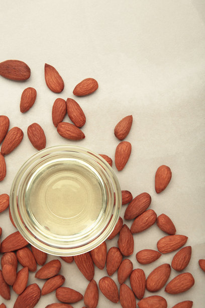 玻璃碗中的杏仁油和杏仁，背景为浅色。竖版照片图片下载