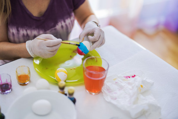 女人在黄色盘子上用刷子和五颜六色的染料手绘复活节彩蛋，颜色鲜艳的蓝色和粉色。瑞典。图片下载