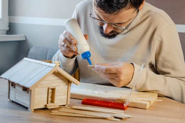 创意男士正在用木棍粘合制作一个小型木屋模型，展现了创造力和工艺技巧 - 股票照片图片下载