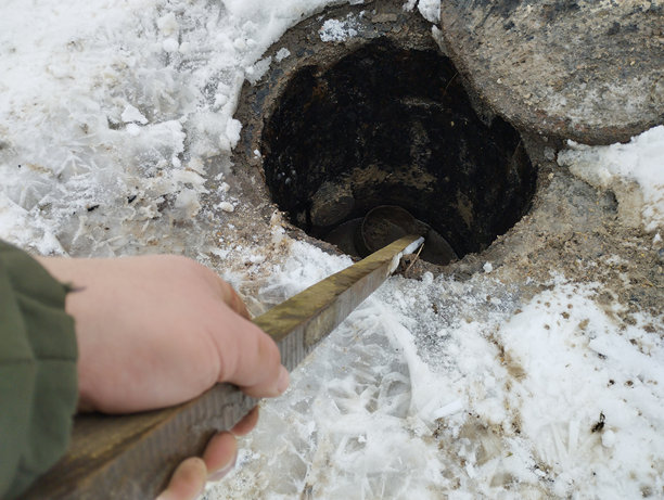 在照片中，一个人使用长棍清理堵塞的下水道。清理下水道井盖的过程。图片下载