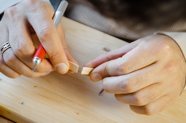 戴眼镜的创意工匠正在木板上制作模型，一个微型木屋，他正在切割材料 - 特写 - 库存照片图片下载
