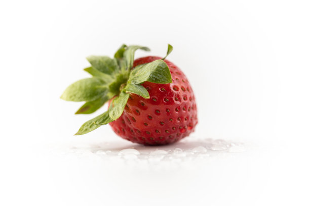 在白色照片背景中央，静静躺着一颗成熟的草莓，背景上有水滴，健康的维生素，季节性的夏季水果，富含维生素C，绿色的草莓蒂像一顶皇冠。图片下载