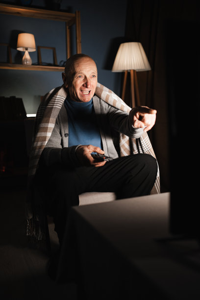 孤独的退休老人晚上独自在家看电视，感到愤怒和恼火，强烈批评他所看到的内容，手指指向屏幕。图片下载