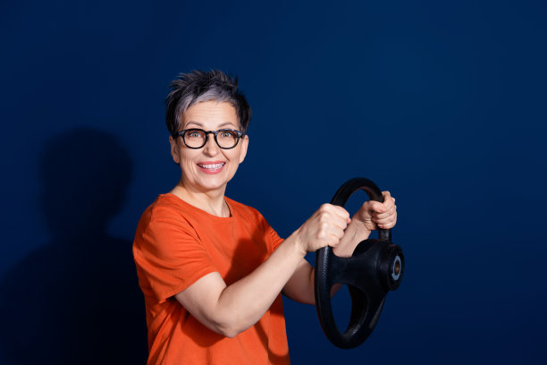 穿着时尚橙色服装的美丽退休女性在深蓝色背景下驾驶汽车的照片肖像图片下载