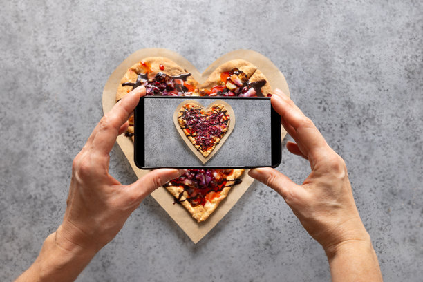 女人的手拍摄情人节甜蜜披萨的照片。图片下载