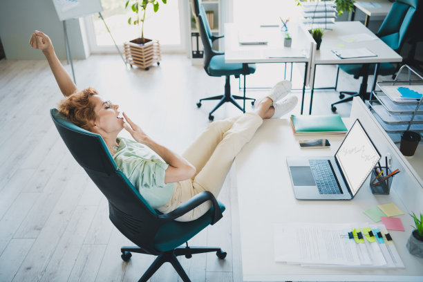 高角度视图照片，成功的年轻女商人坐在椅子上伸展打哈欠，穿着衬衫，现代室内办公室环境。图片下载