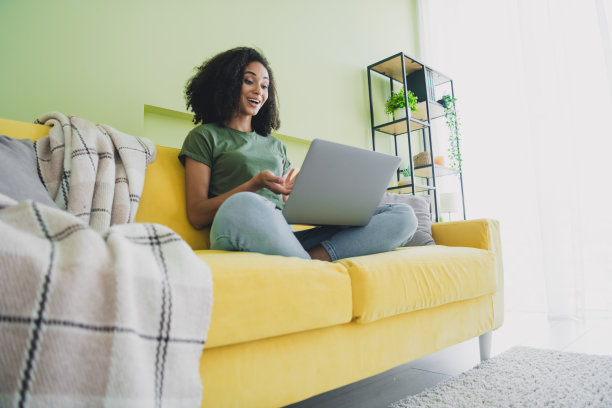 年轻漂亮的女性在室内公寓的绿色客厅里通过笔记本电脑进行视频通话的全身照片图片下载