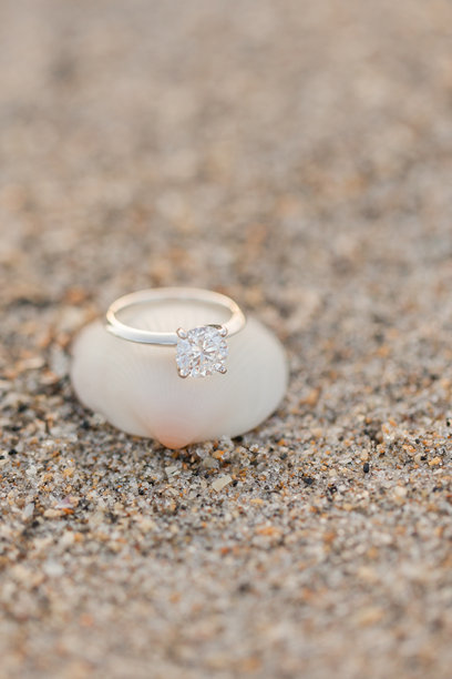 白金圆形钻石订婚戒指的特写照片，放在沙滩上的海螺上图片下载