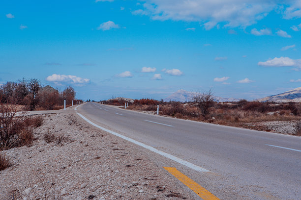 低角度视图的沥青道路，带有黄色条纹。适合自然爱好者、风景摄影和旅游网站的道路视角，背景为蓝天和白云。高质量照片。图片下载