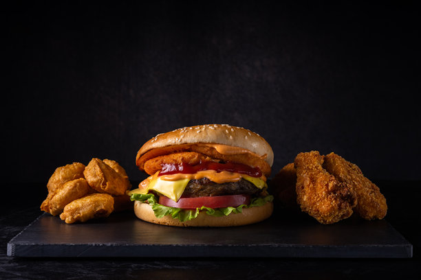 黑色切菜板上的快餐组合，背景为柔和的灰黑色渐变光斑和留白。大肉菜汉堡和鸡肉。艺术感的暗色照片。侧面视角。图片下载