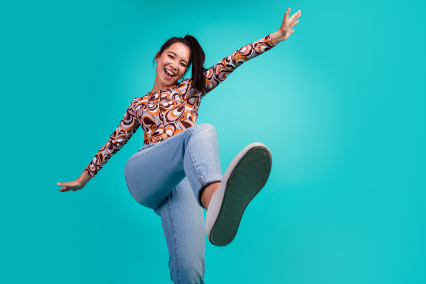 年轻女士在青色背景下穿着时尚多彩的衣服，快乐地跳舞的照片肖像图片下载