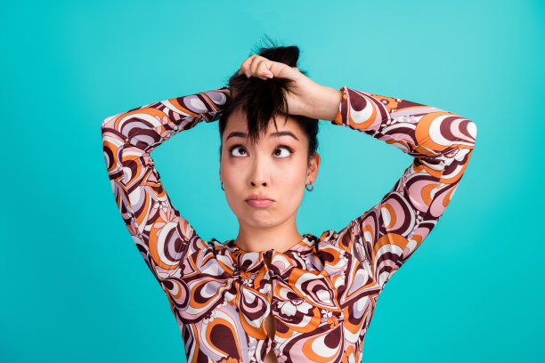 漂亮年轻女孩的照片肖像，表情困惑而惊讶，头发时尚，穿着色彩缤纷的衣服，背景为青色。图片下载