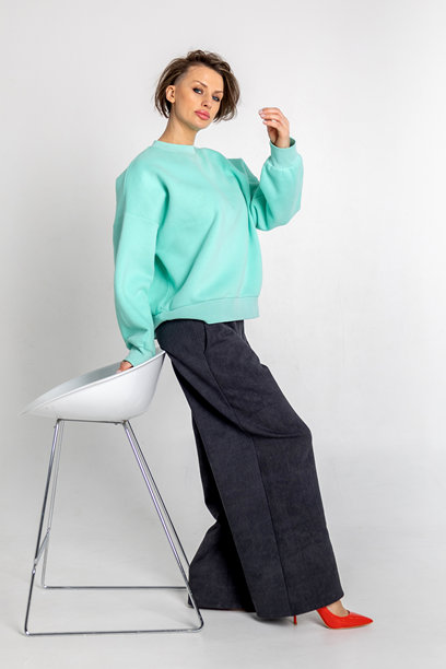 模特外貌的美丽女性肖像。女孩穿着薄荷色毛衣、黑色裤子和红色鞋子，背景为灰色。时尚妆容的漂亮女性在摄影棚中摆姿势。竖版照片图片下载