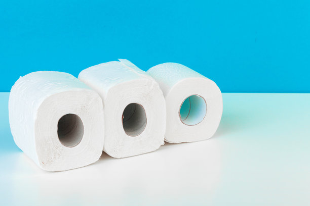 三卷卫生纸孤立在白色桌子上，背景为蓝色。创意照片。图片下载