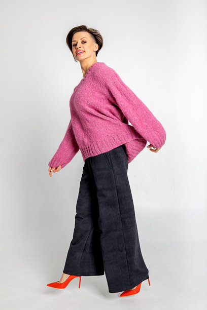 模特外貌的美丽女性肖像。女孩穿着粉色毛衣、黑色裤子和红色鞋子，背景为灰色。时尚妆容的漂亮女性在摄影棚中摆姿势。竖版照片图片下载