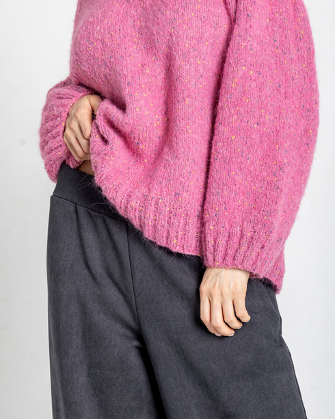 模特外貌的美丽女性肖像。女孩穿着粉色毛衣和黑色裤子，背景为灰色。时尚妆容的漂亮女性在摄影棚中摆姿势。竖版照片图片下载