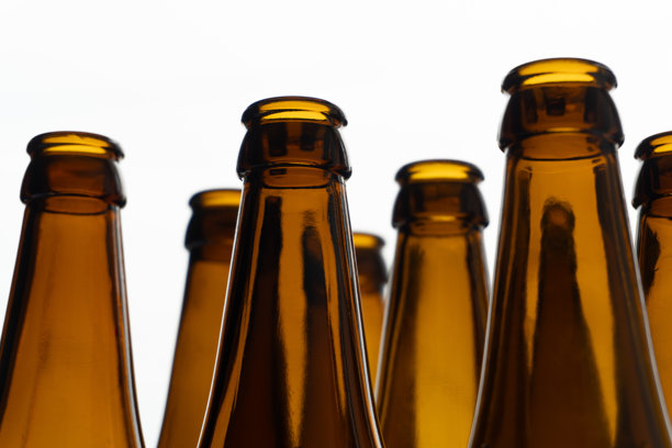 一张极简风格的照片，展示了一排棕色啤酒瓶，反射的玻璃表面在柔和的光线下闪耀。图片下载