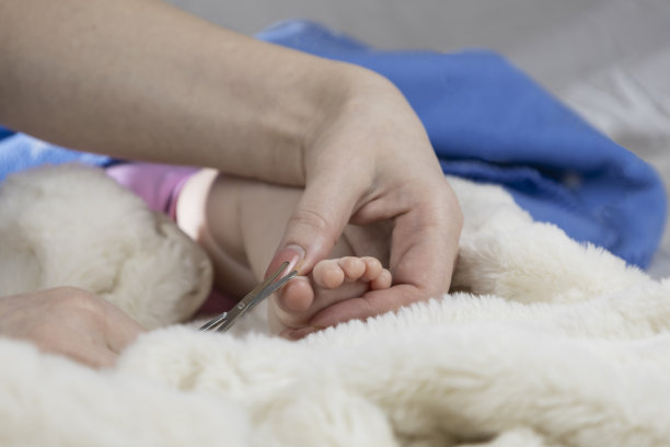 妈妈用婴儿剪刀给宝宝修指甲。特写照片显示母亲的手握着婴儿的脚和指甲剪。图片下载