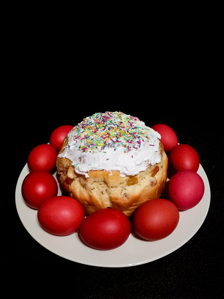 复活节蛋糕面包库里奇，装饰着五彩缤纷的糖屑，旁边放着鲜红的彩蛋，标志着节日庆祝。垂直手机照片图片下载