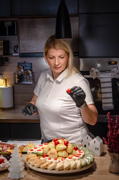 一位年长女性戴着黑手套正在为宴会食品板添加新鲜樱桃番茄 - 股票照片图片下载