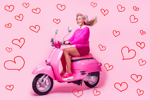 穿着毛衣的兴奋女孩骑着摩托车，急匆匆地在粉色背景下拍摄的全身照片图片下载