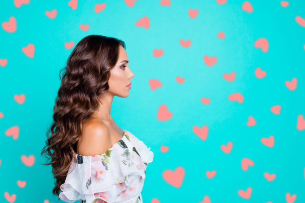 侧面肖像照片，展示了一位严肃自信的卷发棕发女性，拥有现代发型，背景为闪亮的青绿色，留有文本空白。图片下载