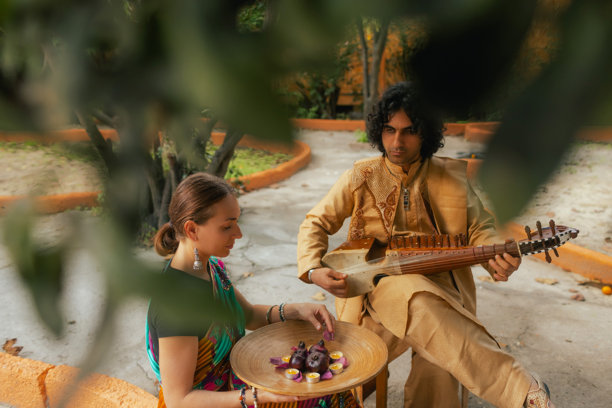 身穿传统服装的印度音乐家在户外家中演奏西塔琴，庆祝节日季节。一位身穿传统纱丽的女性在排灯节期间点燃迪亚灯。快乐的问候照片。系列的一部分。图片下载