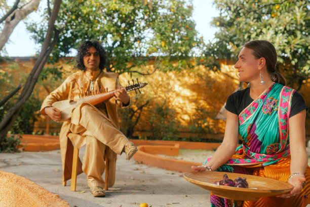 身穿传统服装的印度音乐家在户外家中演奏西塔琴，庆祝节日季节。一位身穿传统纱丽的女性在排灯节期间点燃迪亚灯。快乐的问候照片。系列的一部分。图片下载