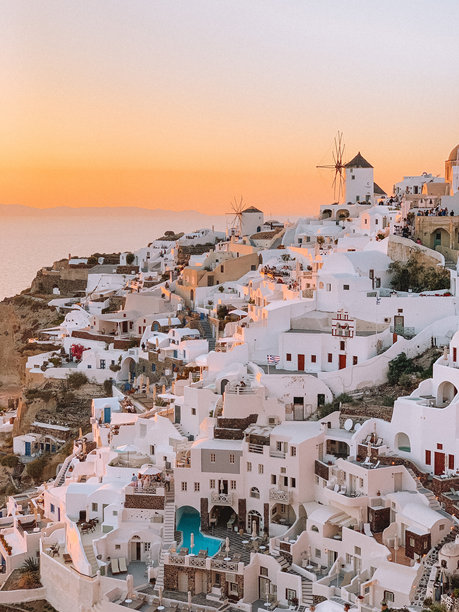 令人惊叹的圣托里尼日落照片，捕捉到温暖的金色天空在太阳落下时，映衬着岛上标志性的白色建筑和蓝色圆顶。图片下载