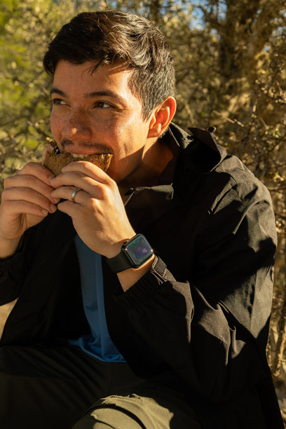 年轻男子坐在山上吃三明治，四处张望的竖版图片图片下载