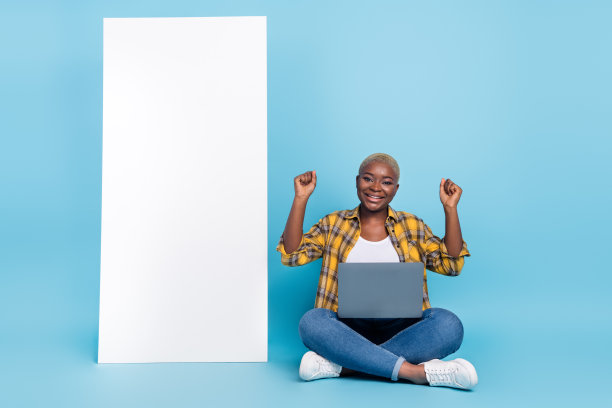 兴奋的幸运女性穿着格子衬衫，手持小工具，站在空旷的蓝色背景前的全身照片图片下载