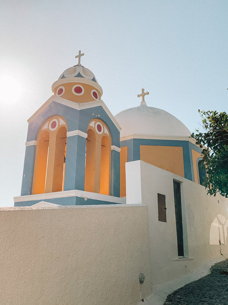 圣托里尼日落前的田园风光照片，捕捉到伊亚标志性的白色建筑和蓝色圆顶在金色时光中温暖地闪耀。图片下载