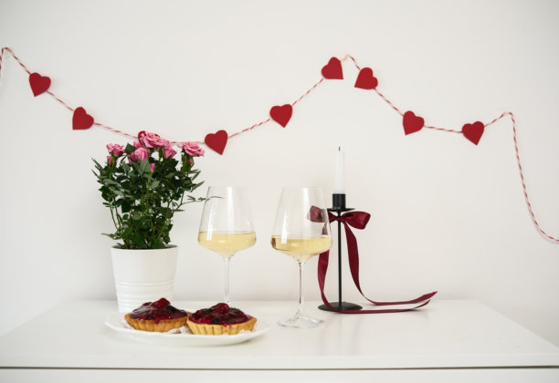 情人节桌面布置，红玫瑰和酒杯，蜡烛，白色背景上的水果蛋糕盘。情人节贺卡 - 图片图片下载